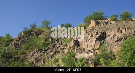 Un pendio roccioso di una cava di granito abbandonata nella regione di Nikolaev in Ucraina in una calda giornata estiva. Pietre affilate sopravite con vegetazione sparsa. Blu Foto Stock