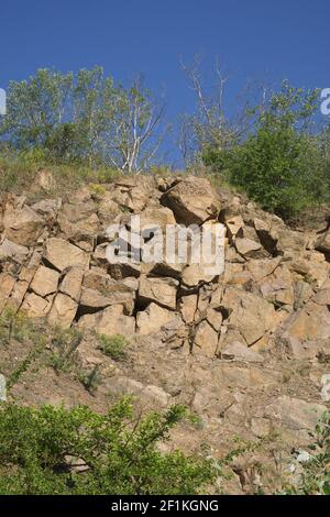 Un pendio roccioso di una cava di granito abbandonata nella regione di Nikolaev in Ucraina in una calda giornata estiva. Pietre affilate sopravite con vegetazione sparsa. Blu Foto Stock