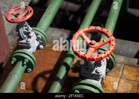 Due valvole verdi petrolchimiche industriali di tipo retrò si chiodano messa a fuoco selettiva sul volante rosso montato con collegamento a flangia acceso Foto Stock