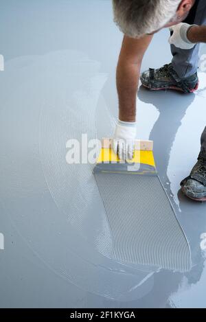 Il lavoratore di costruzione rinnova il pavimento del balcone e diffonde la resina impermeabile e. incollare prima di scheggiare un Foto Stock