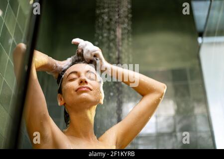 Donna felice con gli occhi chiusi in doccia sciacquare lo shampoo con acqua che gocciola sul viso. Fare la doccia e rilassarsi sotto l'acqua corrente calda. Spazio di copia. Foto Stock
