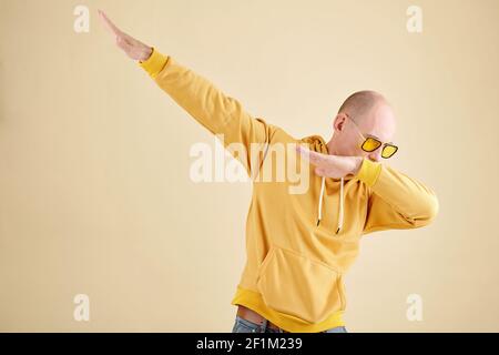Studio ritratto di calvo uomo maturo in giallo felpa con cappuccio dabbing gesto quando si ama ballare da solo Foto Stock