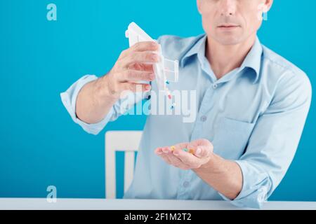 Immagine ritagliata dell'uomo che riempie la mano con una dose settimanale di pillole e supplementi Foto Stock