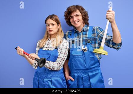 idraulici che tengono il pistone nelle mani, pronti a riparare lavello e bagno, sono riusciti a fare molte cose e riparare molti oggetti. caucasici uomo e donna in b Foto Stock