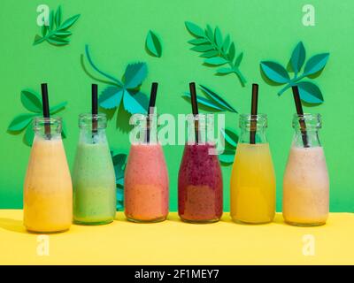 bottiglie di vari smoothies colorati di banana e di bacche su verde sfondo foglio di carta Foto Stock
