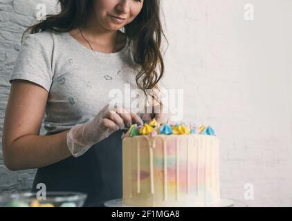 Un pasticciere fa una torta di nozze con le sue mani e mette decorazioni colorate sulle torte con crema. Preparazione alla celebrazione Foto Stock