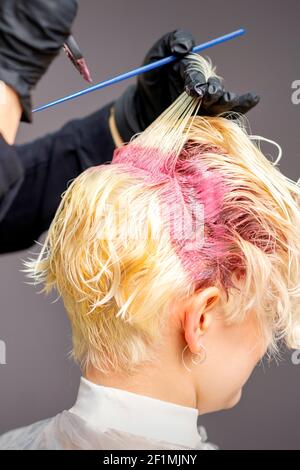 Primo piano delle mani del parrucchiere che applicano il colorante rosa su donna capelli biondi in un parrucchiere Foto Stock