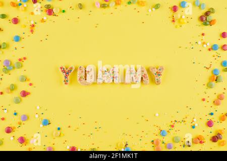 Parola yummy reated con biscotti dolci di zucchero e decorato con piccole caramelle colorate, vista dall'alto Foto Stock