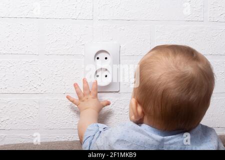 Un ragazzo caucasico irriconoscibile sta giocando con una presa elettrica aperta. Cavi per bambini. Giochi pericolosi con presa elettrica aperta. Foto Stock