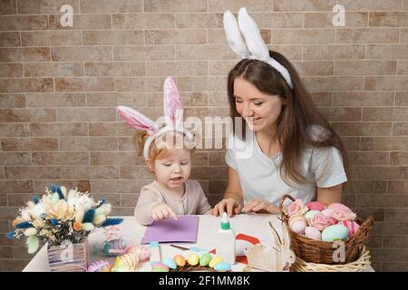 Pasqua, famiglia, vacanza e concetto di bambino - close up della bambina e madre colorare le uova per la pasqua Foto Stock