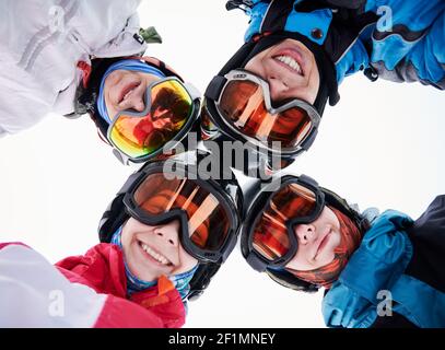 Primo piano di amici felici sciatori in occhiali da sci che toccano le teste ed esprimono emozioni positive. Gruppo di persone gioiose che indossano caschi e occhiali da sci. Concetto di amicizia e sci. Foto Stock