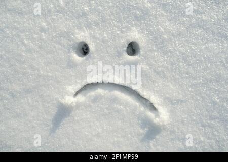 Triste volto smiley disegnato nella neve in una giornata di sole inverno. Spazio di copia. Emozioni negative. Foto Stock