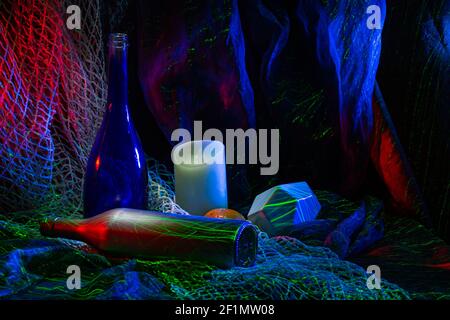 Composizione e luce con oggetti nello studio fotografico. Le bottiglie e le candele sono illuminate in rosso, blu e verde. Foto Stock