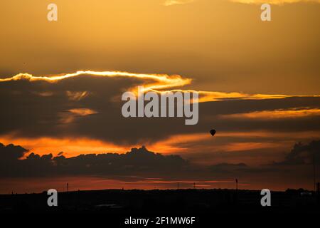 Mongolfiera che sorvola la città alla luce del tramonto. Le nuvole sono evidenziate, la luce è calda. La silhouette del palloncino viene persa nelle nuvole Foto Stock