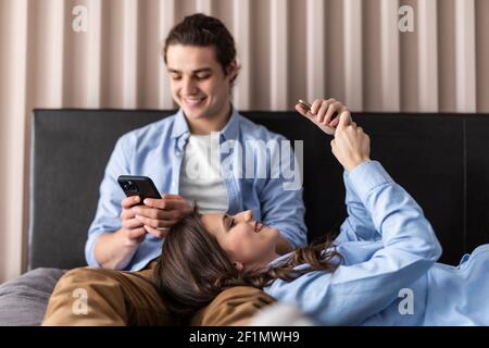 Arrabbiato giovane ognuno con i propri cellulari sdraiato sul letto di casa Foto Stock