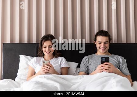 Arrabbiato giovane ognuno con i propri cellulari sdraiato sul letto di casa Foto Stock