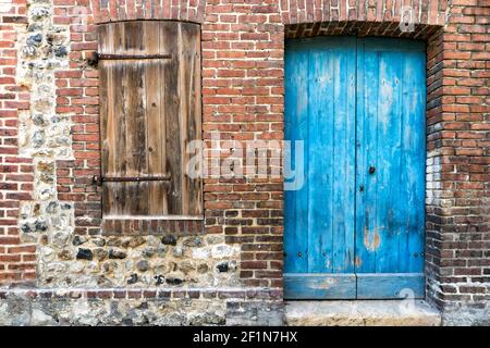 Dettaglio architettonico di una vecchia casa in mattoni e pietra con portone e serranda colorati in legno Foto Stock