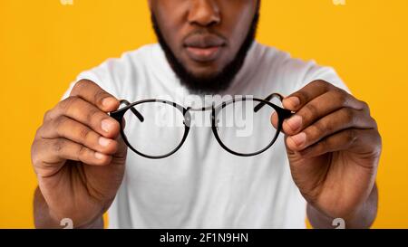 Vista scarsa. Irriconoscibile African Man Holding vetri che hanno problemi di vista difettoso che si pongono sopra Yellow Studio sfondo, ritagliato. Fuoco selettivo su e Foto Stock