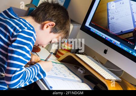 Istruzione a distanza, imparare a casa durante la pandemia COVID-19. Bambino ragazzo che scrive lettere davanti al computer, Ungheria, Europa Foto Stock