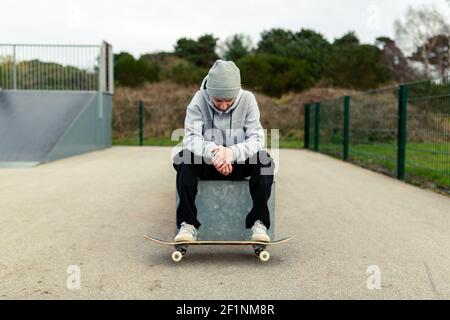 Ritratto di un giovane adulto maschio con uno skateboard seduto su una scatola in uno skatepark locale. Skateboard concetto di stile di vita sano Foto Stock