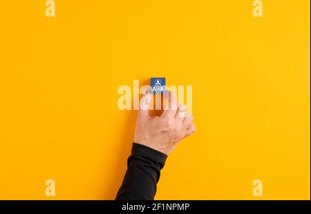 La mano maschile tiene un cubo di legno blu con l'icona della squadra dei dipendenti su sfondo giallo. Lavoro di squadra aziendale o concetto di team building Foto Stock