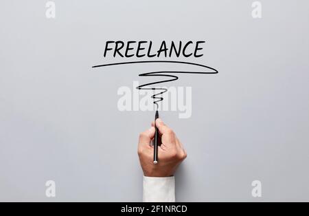 Uomo d'affari mano che scrive freelance su sfondo grigio. Lavoro freelance o lavorando come concetto freelance.. Foto Stock