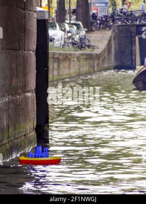 Una piccola barca giocattolo in plastica di colore rosso, blu e giallo perso in un canale d'acqua ad Amsterdam. Foto Stock