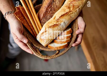 Chiudere un yp di mano dell'uomo, tenendo il cestello con vari tipi di pane appena sfornato. Primo piano concetto di pane fatto in casa, piccola panetteria, prodotti naturali della fattoria, locale Foto Stock