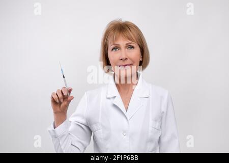 Ritratto di medico femminile maturo in siringa di tenuta di camice da laboratorio con farmaco, vaccino o iniezione di bellezza su sfondo studio chiaro. Cosmetologia estetica Foto Stock