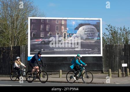 tre ciclisti passano un cartello di avvertimento dell'inquinamento e della minaccia per la salute pubblica causata dal motore al minimo, a twickenham, middlesex, inghilterra Foto Stock