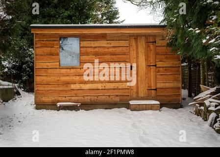 Waney bordo boscoso giardino capannone coperto di neve dopo pesante nevicata Foto Stock