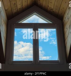 Cielo blu e nuvole bianche viste attraverso un grande dormitorio finestra in un tetto di legno Foto Stock