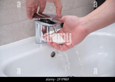 Mani che tengono una barra di sapone e aprono il rubinetto. Processo di lavaggio delle mani. Foto Stock