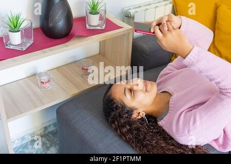 ragazza sorridente tesa sul divano e scrivendo sul cellulare Foto Stock