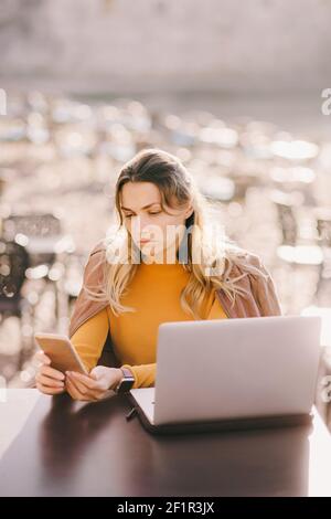 una donna seria lavora su un computer portatile all'aperto in un bar Foto Stock