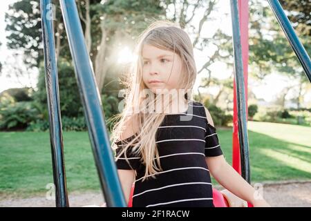 Giovane ragazza in piedi su un altalena in un parco giochi pubblico Foto Stock