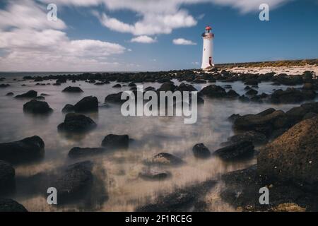 Port Fairy Lighthouse sull'isola di Griffiths, bassa marea in primo piano, onde sullo sfondo, Victoria, Australia. Foto Stock