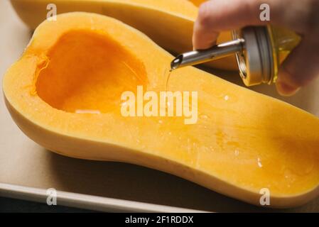 Versare l'olio d'oliva su una zucca di butternut a metà Foto Stock