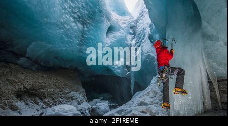 L'uomo arrampica icicle all'interno della grotta del ghiacciaio in Islanda Foto Stock