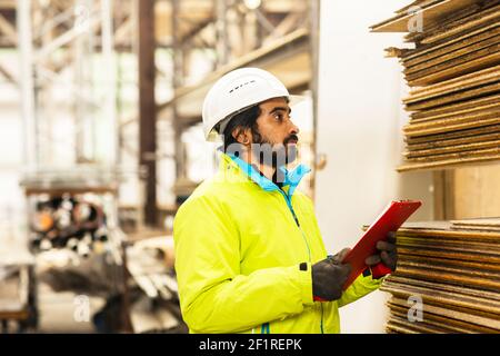 Giovane lavoratore con casco e barba che lavora in un magazzino Foto Stock