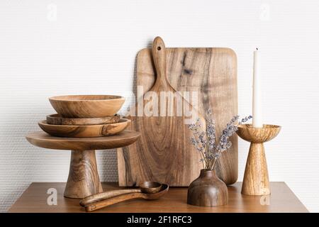 utensili da cucina in legno contro parete bianca. Tavole, cucchiai, ciotole, stativo per torte, candelabro e vaso. Foto Stock