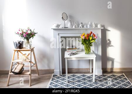 Bouquet di tulipani colorati in un vaso in vetro figurato su una console camino bianca. Una fairence figurine di angelo come decorazione interna. Spazio di copia. Foto Stock