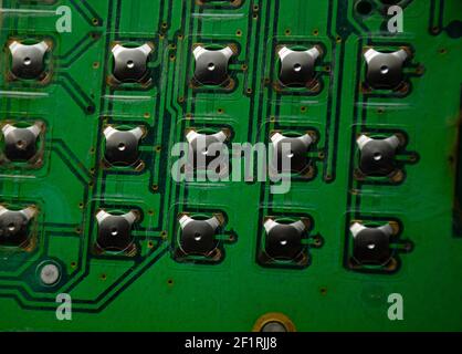 Piazzole di contatto circolari per pulsanti della parte inferiore di una scheda a circuito stampato. Closeup del circuito flessibile elettronico. Astratto background tecnico. Verde trasparente Foto Stock