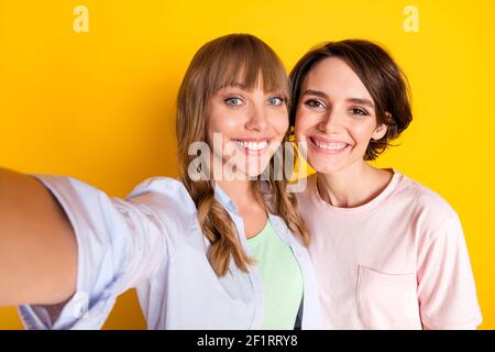 Ritratto di due bellissime Signore soddisfatto fare selfie noothy sorriso guarda la telecamera isolata su sfondo giallo Foto Stock