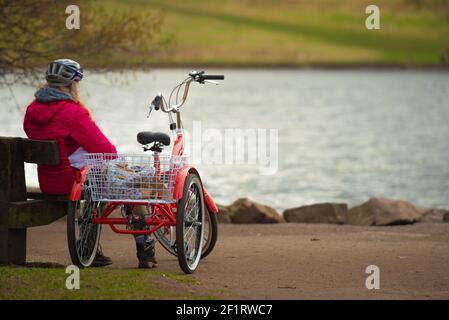 Edimburgo, Scozia, Regno Unito. 8 marzo 2021. Una donna che prende una pausa dal suo triciclo rosso intorno Holyrood Park, seduto a guardare i cigni a St Marg Foto Stock