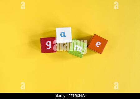 GIOCO - Parola fatta da blocchi di legno colorati. Cubi dipinti con lettere su sfondo giallo. Vista dall'alto. Messa a fuoco selettiva. Spazio di copia. Foto Stock