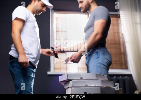 Scatole della pizza nello sfondo sfocato, un uomo di consegna della pizza e un maschio caucasico pagano con una carta di credito. Foto Stock