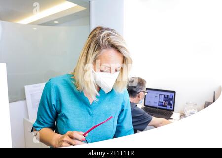 infermiere con maschera e occhiali in mano, personale in background presso la reception dell'ospedale dentale Foto Stock