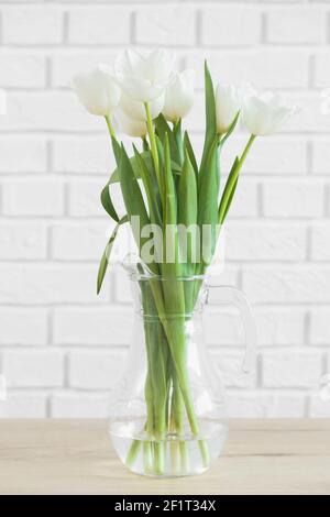Tulipani bianchi in vaso di vetro su fondo parete di mattoni bianchi Foto Stock
