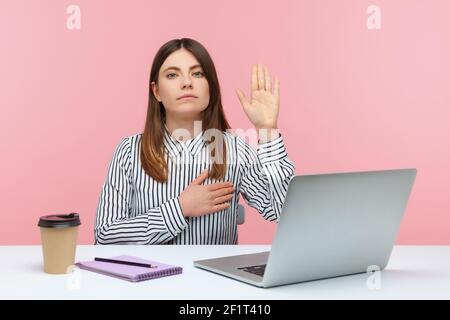 Giuro! Donna onesta lavoro dedicato che alza la mano per dare la promessa seduta sul posto di lavoro, giurando con espressione fedele fidata. IND Foto Stock